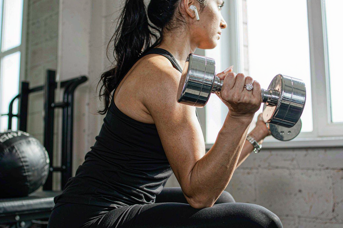 woman wearing moissanite engagement ring while holding dumbbell at gym in natural window light