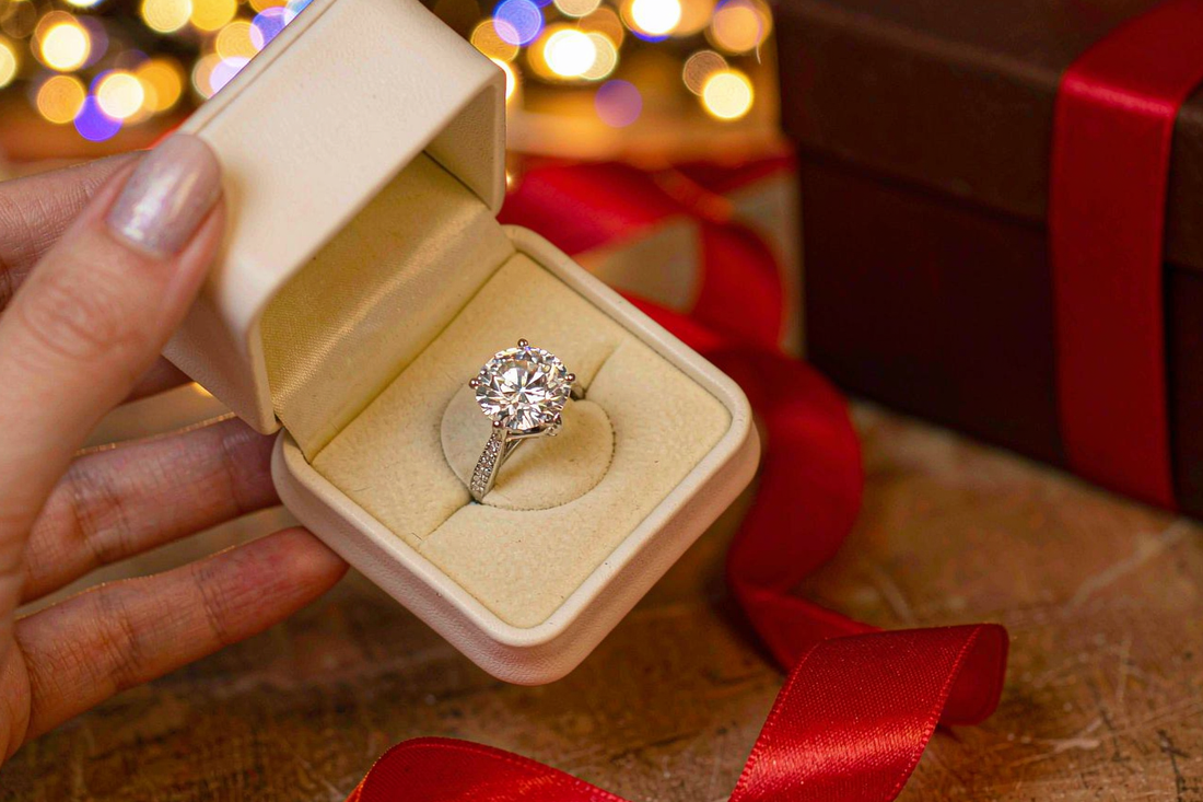 woman's hand holding open jewelry gift box with sparkling moissanite ring and holiday bokeh lights