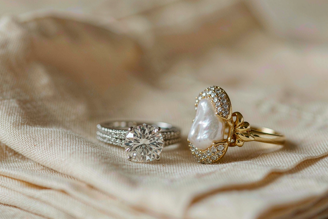 round moissanite solitaire ring and classic pearl ring displayed side by side on cream linen fabric