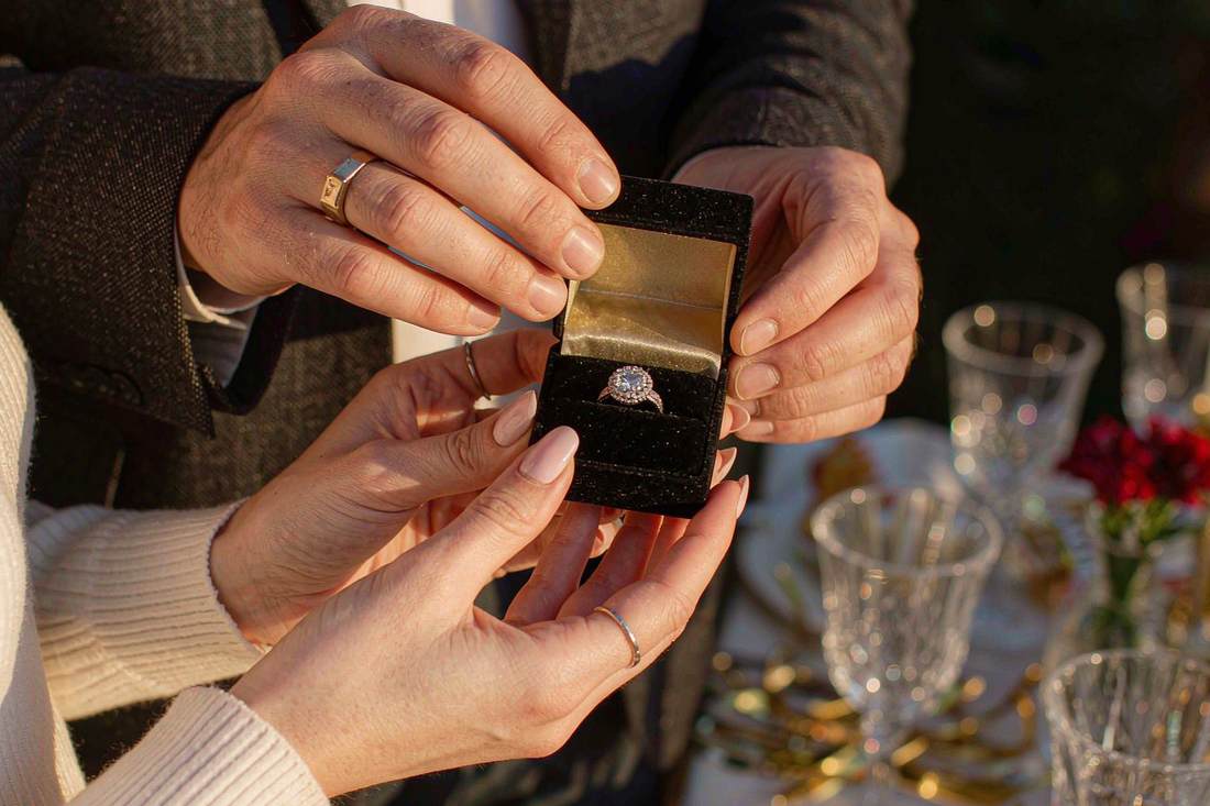 couple's hands exchanging velvet jewelry gift box with moissanite anniversary ring in warm golden light