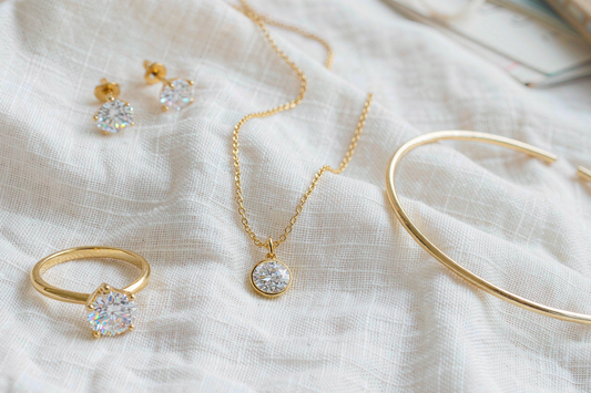 flat lay of honeymoon jewelry capsule including engagement ring dainty gold necklace and stud earrings on white linen