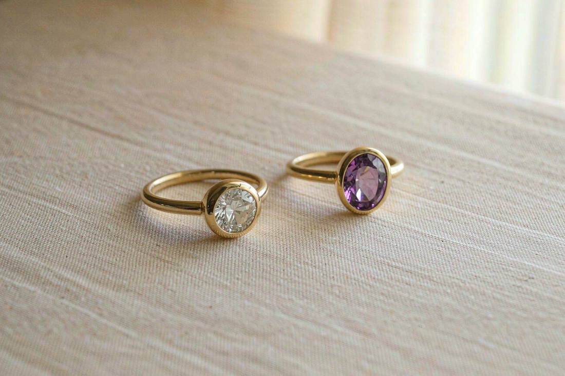 round moissanite solitaire and oval amethyst ring side by side on warm beige linen fabric