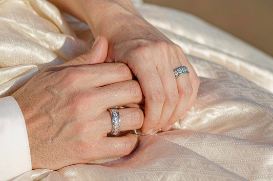 matching couple rings his and hers moissanite bands on intertwined hands on neutral linen